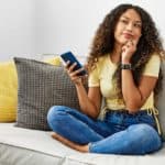 A woman sits on sofa pondering a question.